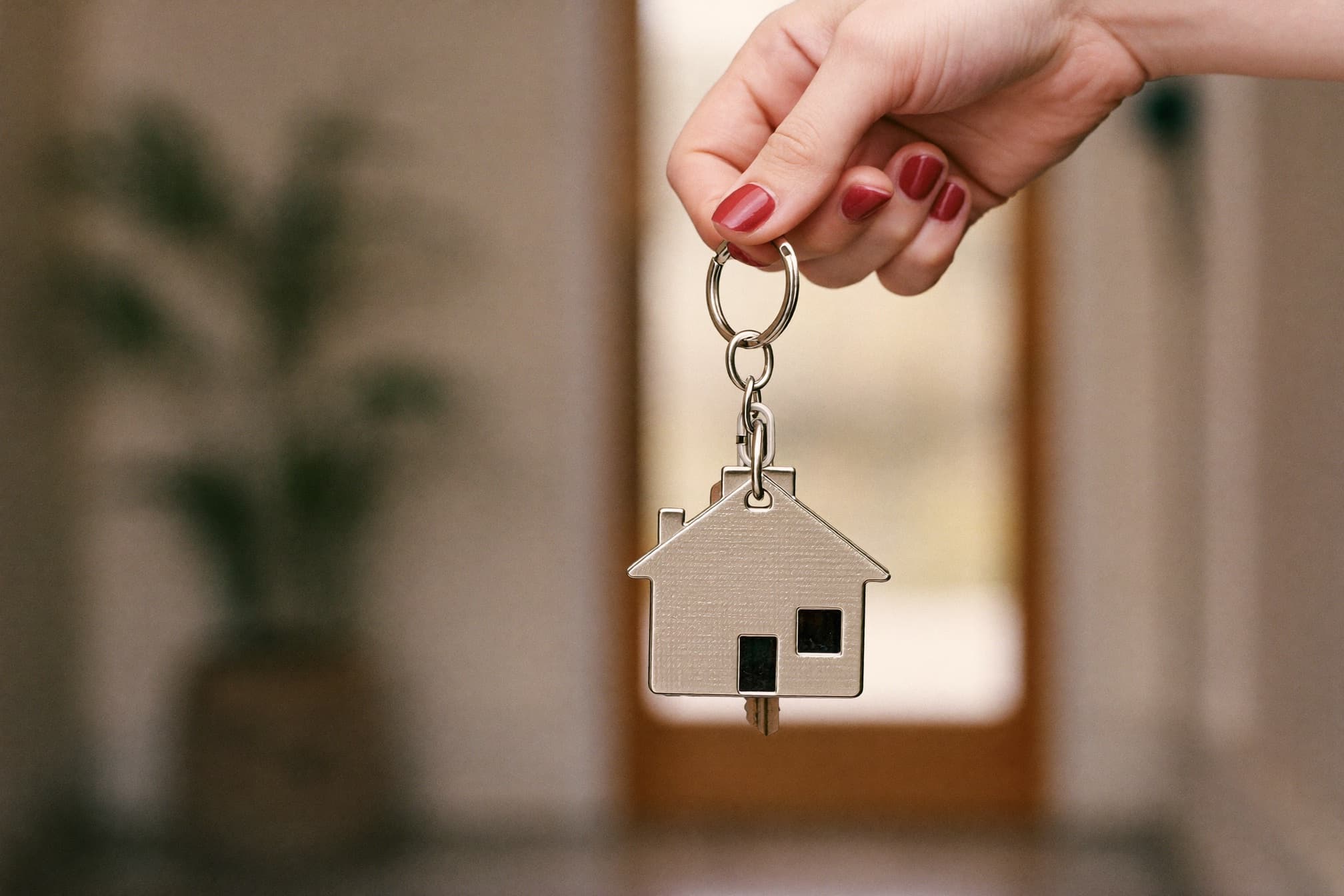 A hand holding house keys with a house-shaped keychain at a front entrance
